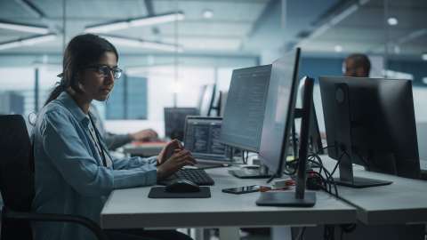 Eine Frau, die in einem Büro an einem Desktop-Computer mit zwei Monitoren arbeitet