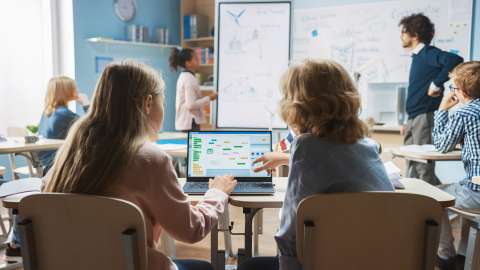 Zwei Schüler in einem Klassenzimmer überprüfen gemeinsam ein Flussdiagramm auf demselben Laptop.