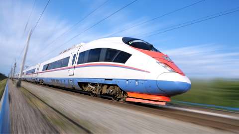Modern aussehender Personenzug in schneller Bewegung auf den Gleisen neben einer landwirtschaftlichen Landschaft