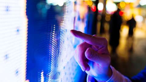 Finger eines Mannes, der nachts auf einen LED-Bildschirm mit Börsenpreisen zeigt